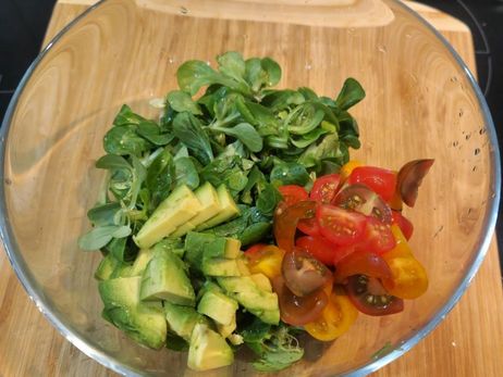 Rezept für ein paniertes Feta-Schnitzel mit Salat: Zupfe und wasche den Feldsalat gründlich und gebe den Salat mit der Avocado und den Tomaten in eine Schüssel.