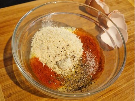 Rezept für ein paniertes Feta-Schnitzel mit Salat: Füge nun den geriebenen Parmesan, Salz, Pfeffer und das Paprikapulver den geschlagenen Eiern hinzu.